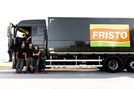 Vier Kollegen stehen vor einem LKW von FRISTO. Alle tragen Arbeitskleidung und lächeln in die Kamera