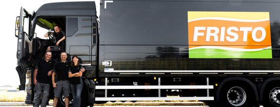 Vier Kollegen stehen vor einem LKW von FRISTO. Alle tragen Arbeitskleidung und lächeln in die Kamera