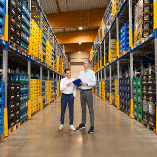 Auf dem Bild zu sehen sind zwei junge, gut gekleidete Mitarbeiter bei der Bestandsaufnahme der Getränke in einem unserer großen Lager, umgeben von der strukturierten Anordnung der Getränke links und rechts.